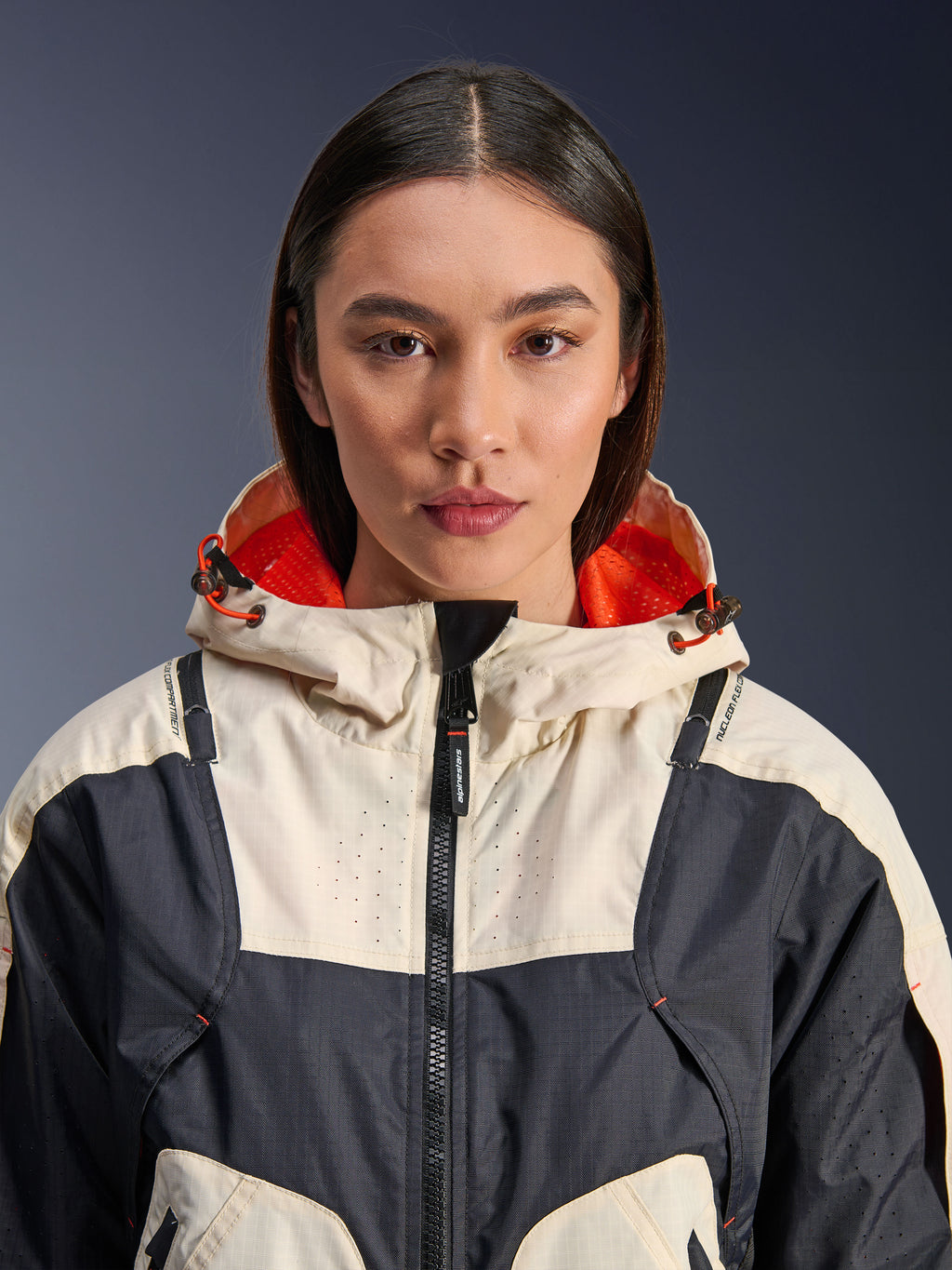 Alpinestars Molly Air Jacket, giacca da moto da donna in tessuto, Black Almond, vista frontale ravvicinata di una modella che indossa la giacca con design a pannelli crema e nero, cappuccio con fodera in rete arancione vivace e dettagli traforati al laser sul petto