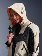 Giacca Alpinestars Molly Air in Black Almond, indossata da una modella con il cappuccio sollevato, caratterizzata da un design color-block crema e nero, fodera in rete arancione vivace ed elementi di design tecnico urbano con logo a stella e dettagli con cerniera.