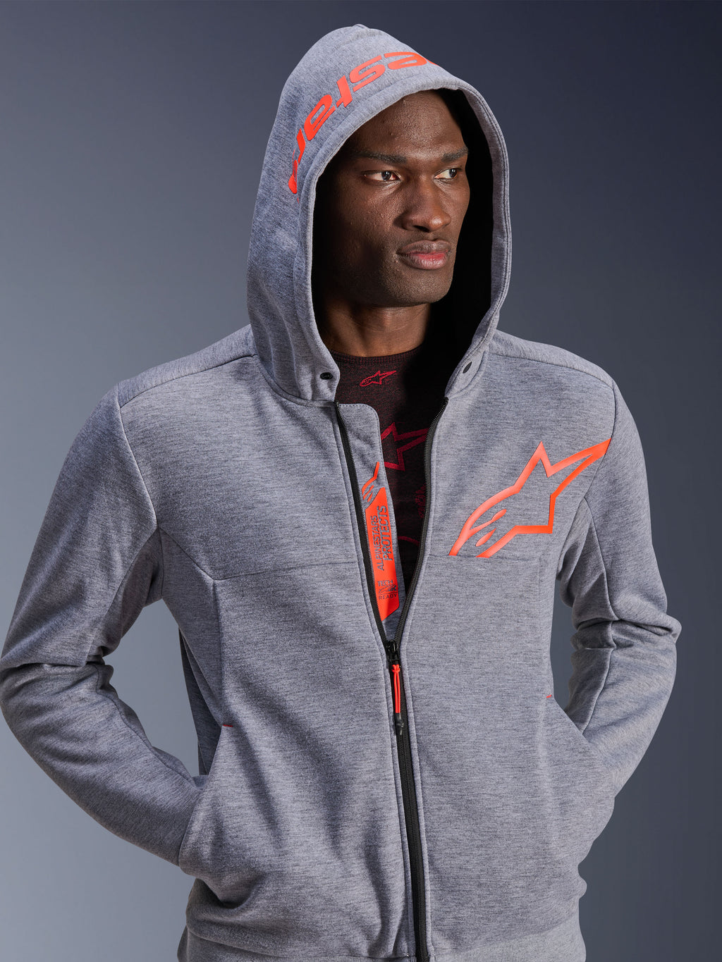 Alpinestars Chrome V2 Sport Hoodie, felpa da moto, grigio melange e rosso fluo, uomo con cappuccio sollevato, con grande logo a stella arancione sul petto e scritta Alpinestars sul cappuccio, design urbano casual
