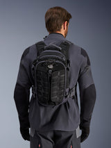 Alpinestars AT-15 Back Pack, zaino da moto adventure, Nero Deep Gray, indossato da una persona sopra una giacca tecnica grigia, vista posteriore con logo 'ALL TERRA', design ergonomico con pannelli rinforzati e cinghie di sicurezza.