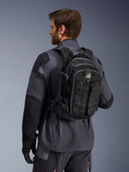 Alpinestars AT-15 Back Pack, zaino da moto adventure, nero e grigio scuro, indossato da un pilota con giacca grigia, caratterizzato da un design tecnico con sistema MOLLE e marchio 'TERRA', equipaggiamento ergonomico per il fuoristrada