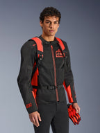 Zaino Alpinestars MM93 AMP3, rosso fluo e nero, indossato da un modello con giacca da moto e guanti MM93 coordinati neri e rossi, vista frontale che mette in risalto gli spallacci regolabili e la fibbia sul petto, equipaggiamento tecnico ispirato alle corse