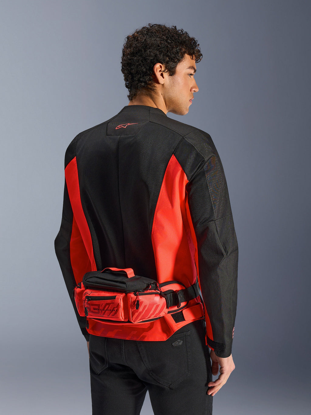 Alpinestars MM93 Waist Bag, borsa a vita da moto, rosso brillante e nero, indossata sopra una giacca da moto coordinata nera e rossa, con scomparti con cerniera e logo Marc Marquez MM93, struttura in tessuto resistente per il motociclismo