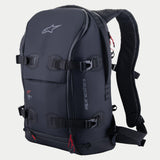 Zaino Alpinestars AMP-7, zaino tecnico da moto, nero con accenti rossi sulle cerniere, dotato di quattro cinghie di compressione regolabili con fibbie, pareti imbottite strutturate, logo Alpinestars superiore e marchio laterale, spallacci ergonomici per adventure e touring stradale.