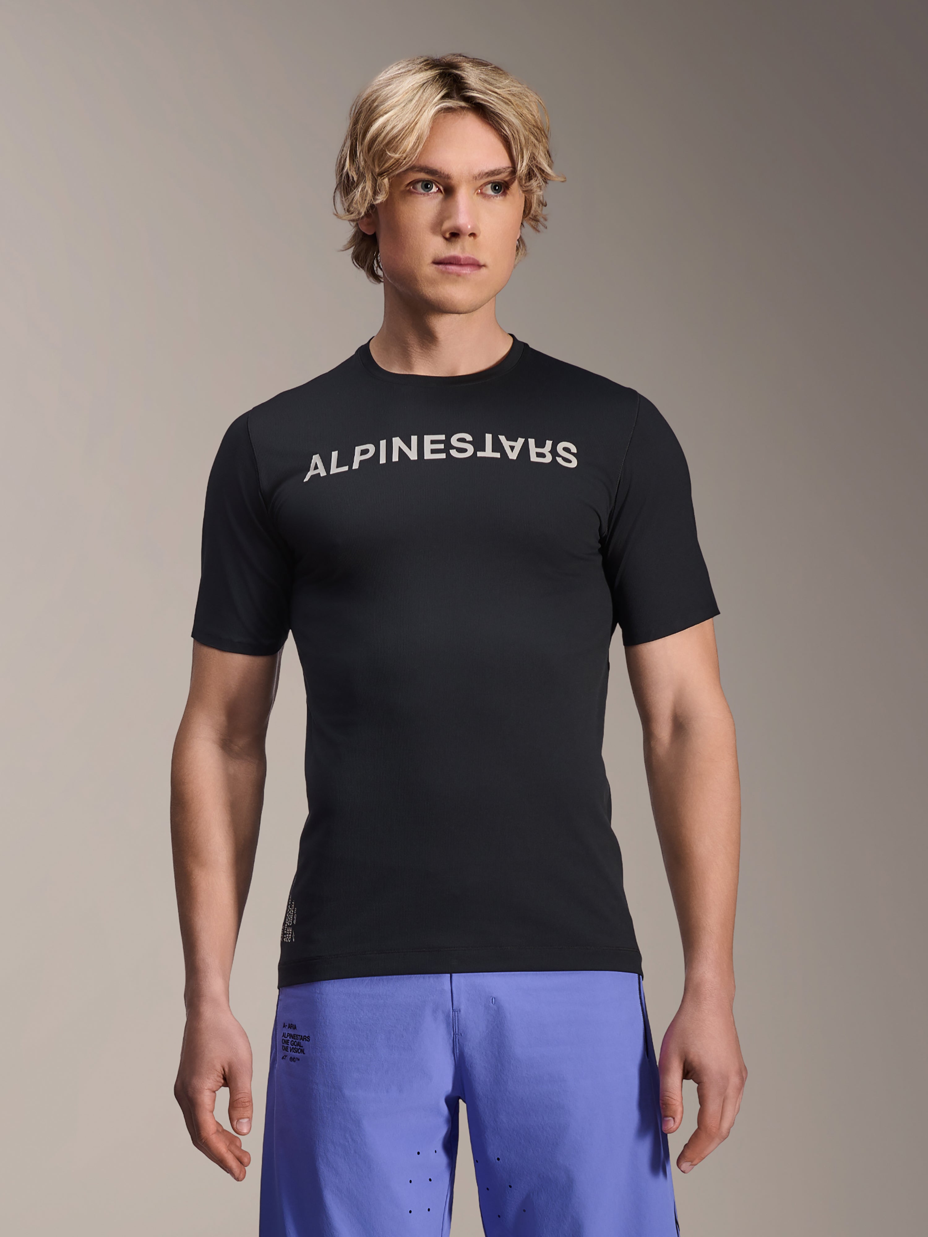 Alpinestars A-Aria Switch Jersey, maglia MTB a maniche corte, nera con scritta Alpinestars bianca sul petto, indossata da un modello con pantaloncini viola, tessuto tecnico leggero per il trail riding
