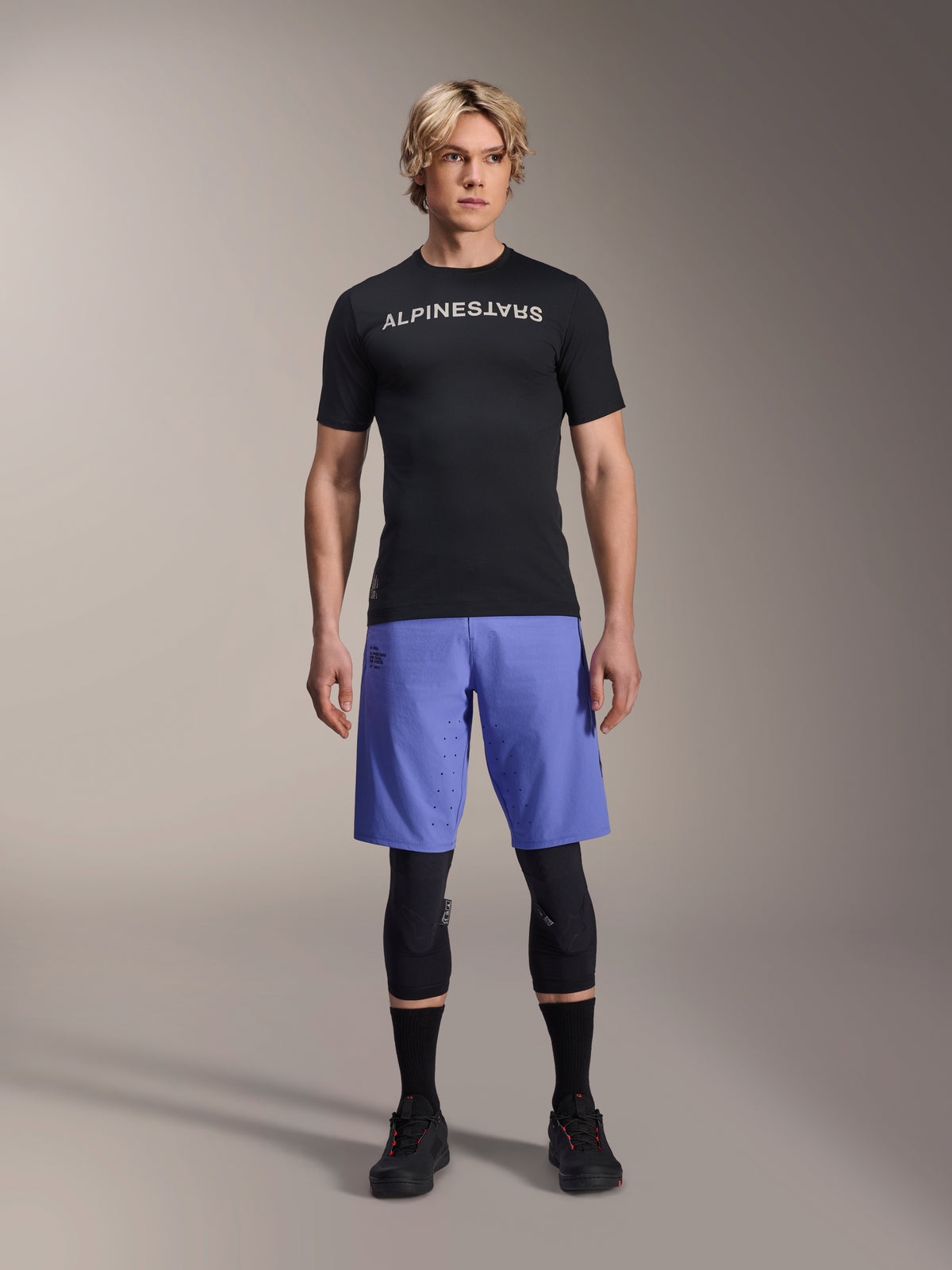 Alpinestars A-Aria Lite Short in Baja Blue, pantaloncini MTB da uomo, indossati con maglia nera a maniche corte e ginocchiere protettive, con perforazioni laser per la ventilazione, abbigliamento tecnico per mountain bike
