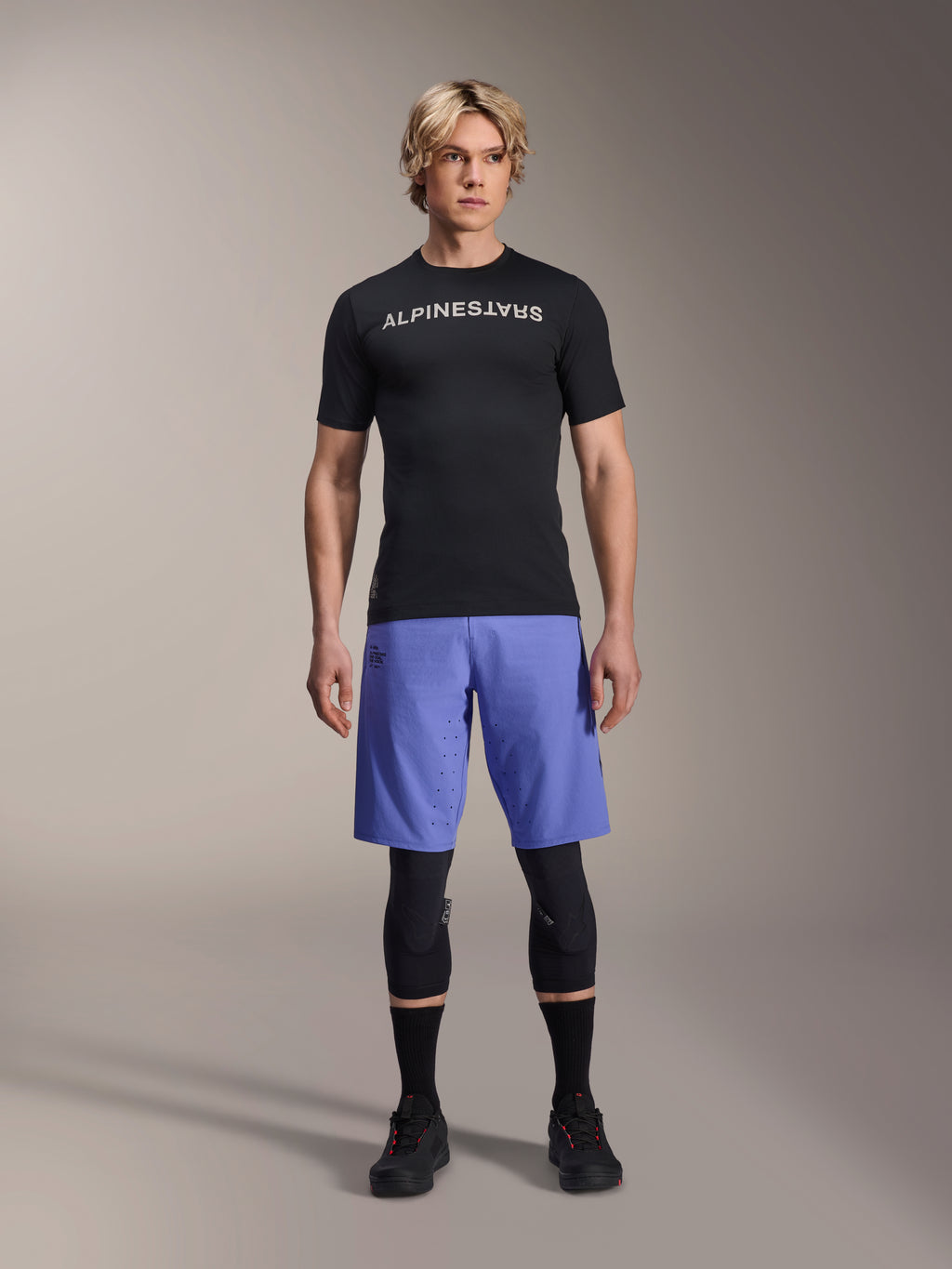 Alpinestars A-Aria Lite Short in Baja Blue, pantaloncini MTB da uomo, indossati con maglia nera a maniche corte e ginocchiere protettive, con perforazioni laser per la ventilazione, abbigliamento tecnico per mountain bike