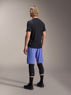Modello visto da dietro che indossa i pantaloncini Alpinestars A-Aria Lite in Baja Blue, abbinati a una maglia nera a maniche corte e protezioni per le ginocchia nere, abbigliamento professionale da ciclismo MTB per trail riding