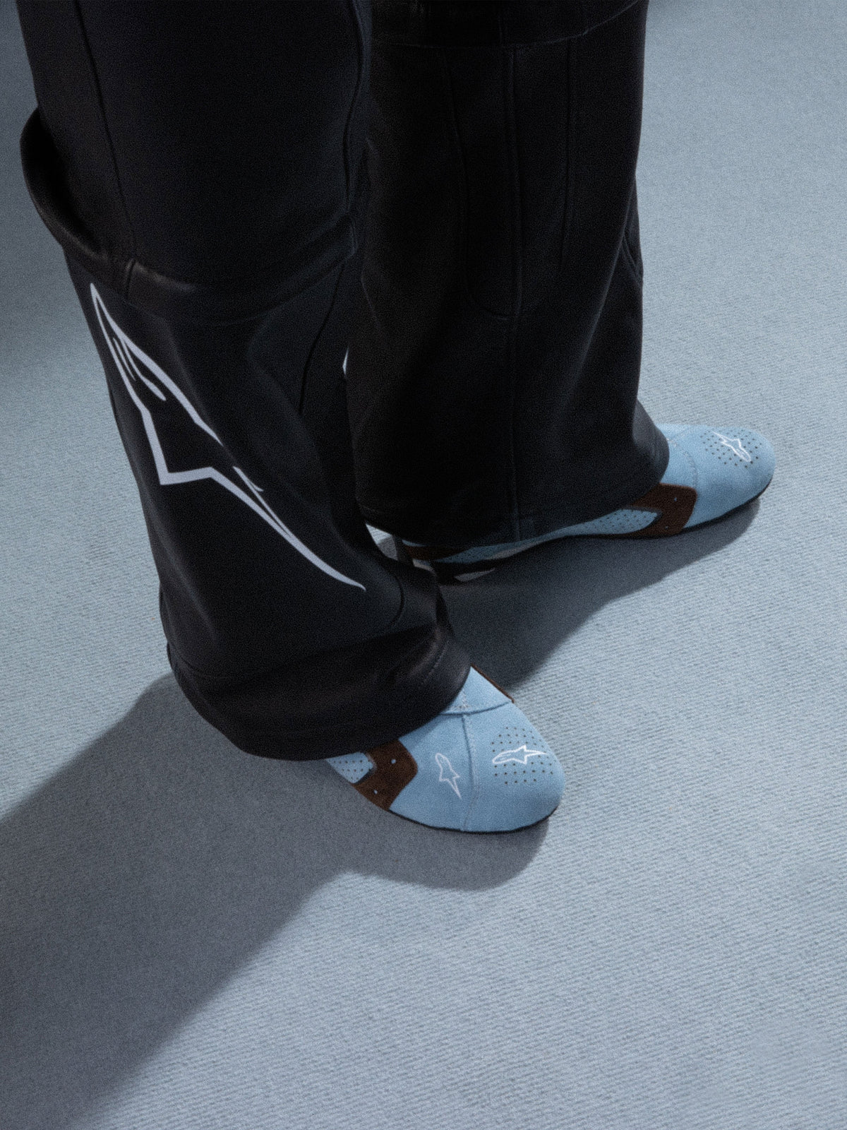 Alpinestars RSRV Starline Shoes, scarpe casual lifestyle azzurre con dettagli marroni, design perforato, logo bianco, indossate con pantaloni in pelle nera con design bianco