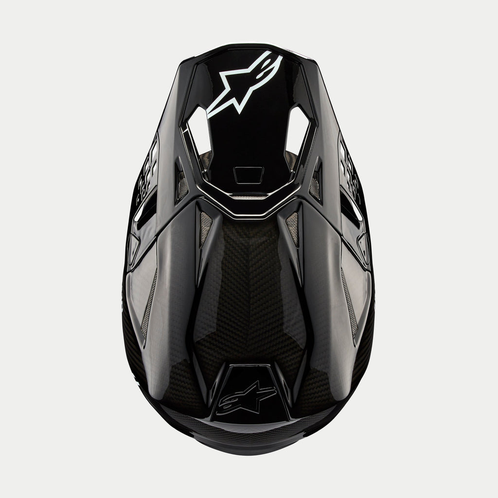 Casco Alpinestars Supertech M10 Solid, casco da motocross, carbonio nero lucido, vista dall'alto con trama in fibra di carbonio a vista, logo Astars bianco sulla visiera, profilo aerodinamico con porte di ventilazione integrate