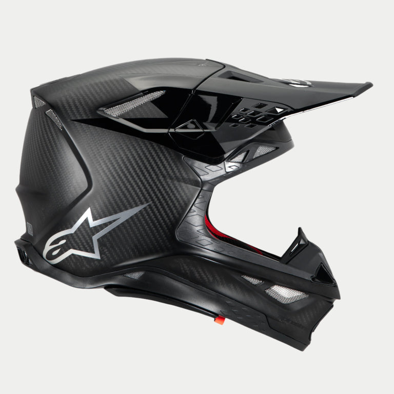 Casco Alpinestars Supertech M10 Fame, casco da motocross, carbonio nero opaco e lucido, profilo laterale che mette in risalto la trama in fibra di carbonio e il logo Astars argento, design aerodinamico con diverse prese d'aria protette da rete, protezione per la testa off-road ad alte prestazioni