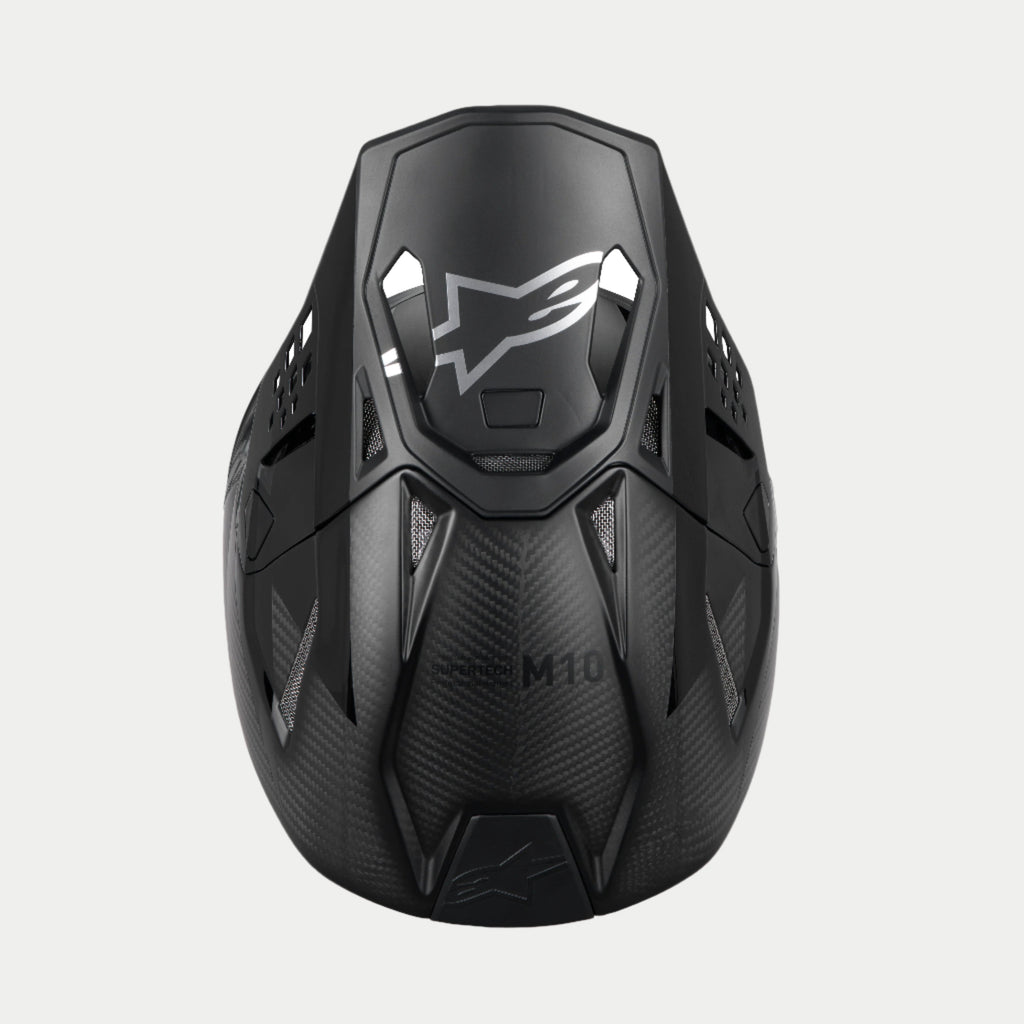 Casco Alpinestars Supertech M10 Fame ECE 22.06, casco da motocross, nero carbonio opaco e lucido, vista dall'alto che mette in risalto la trama in fibra di carbonio, visiera aerodinamica con logo Alpinestars argento e numerose porte di ventilazione per corse off-road.