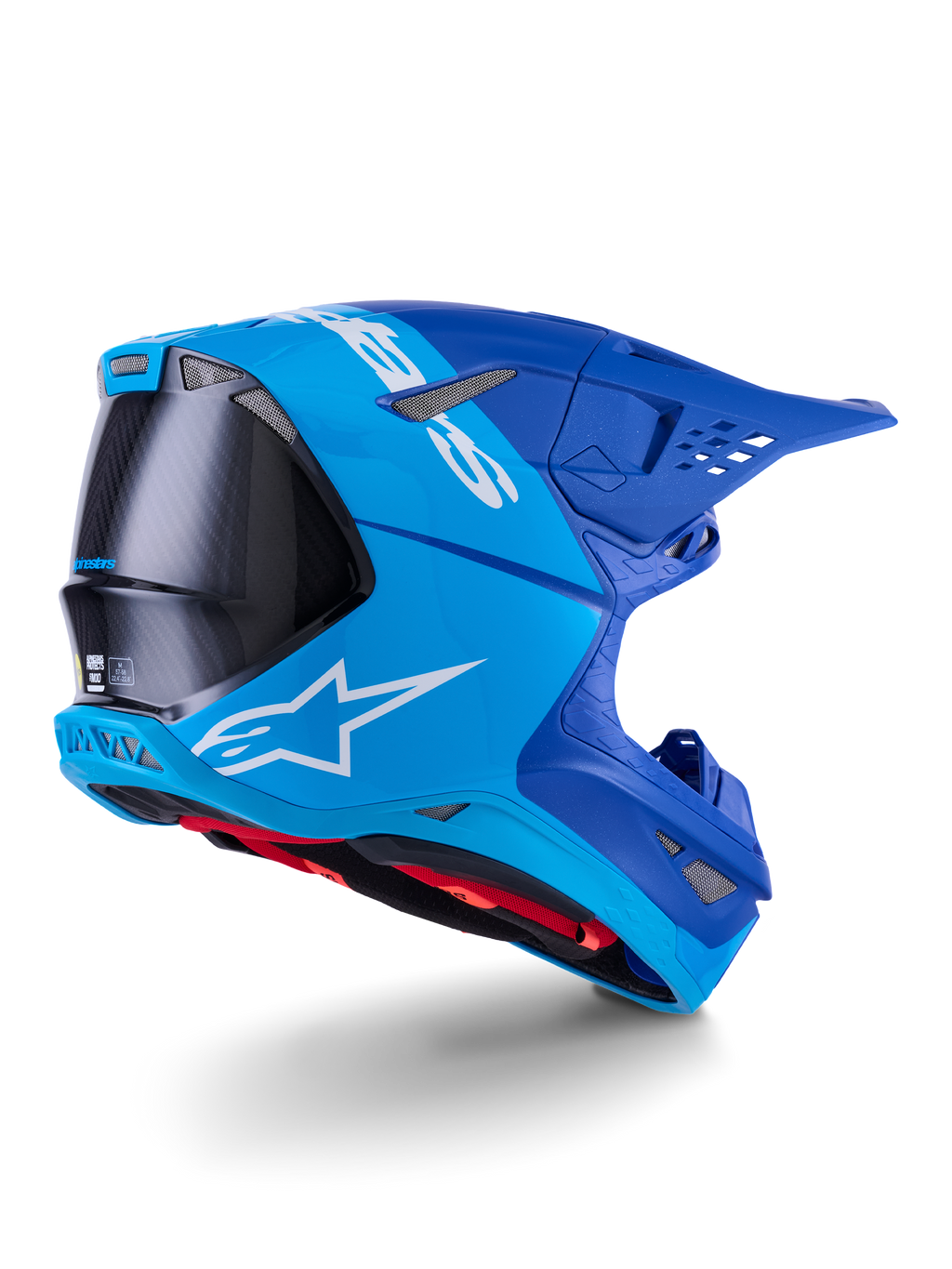 Casco Alpinestars Supertech M10 Flood, casco da motocross, azzurro e blu navy con fibra di carbonio nera a vista, profilo posteriore-laterale che mostra le porte di ventilazione e il logo bianco, interno rosso, design aerodinamico avanzato per prestazioni off-road