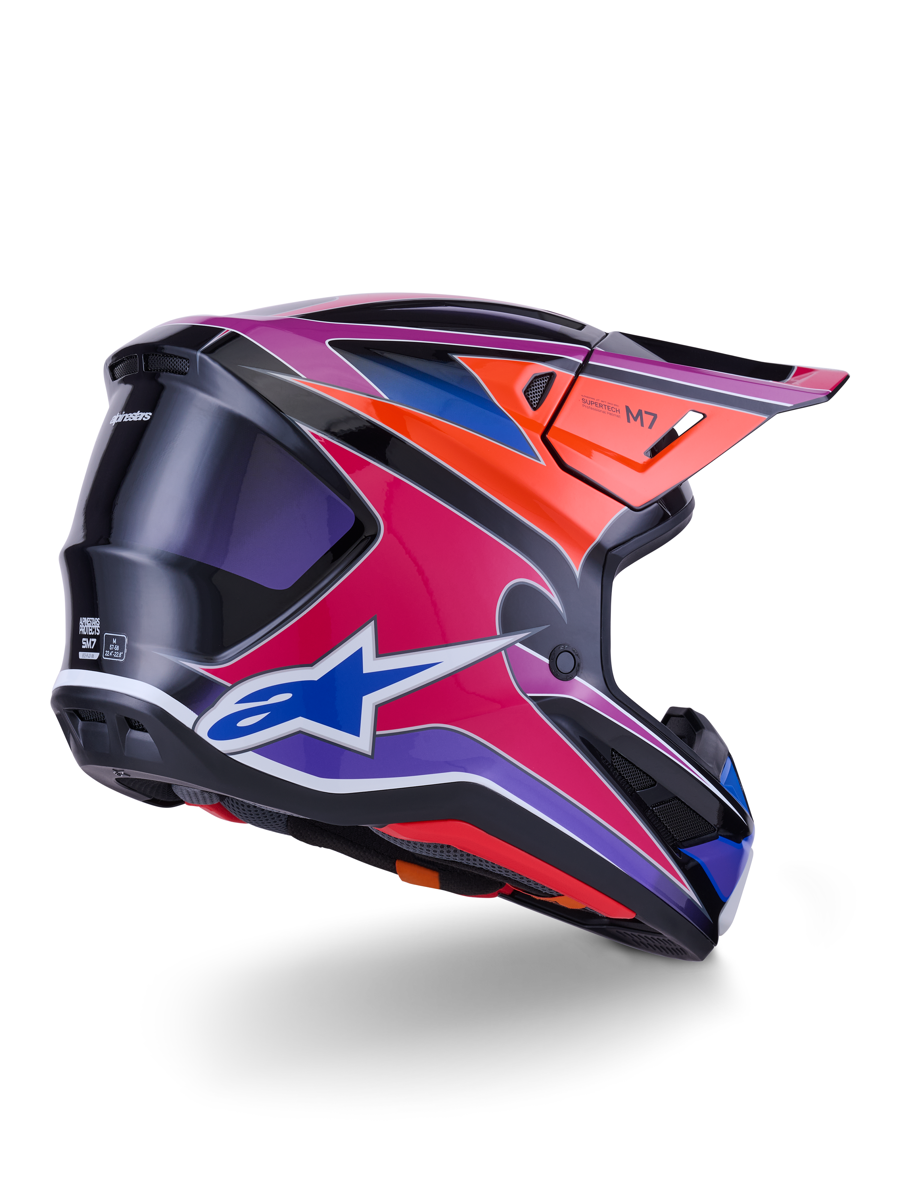 Casco Alpinestars S-M7 Fuse, casco da motocross, finitura lucida blu, viola e rosa con accenti arancioni e neri, vista posteriore a tre quarti che mostra la calotta aerodinamica, la visiera e le prese di ventilazione, protezione professionale per gare fuoristrada