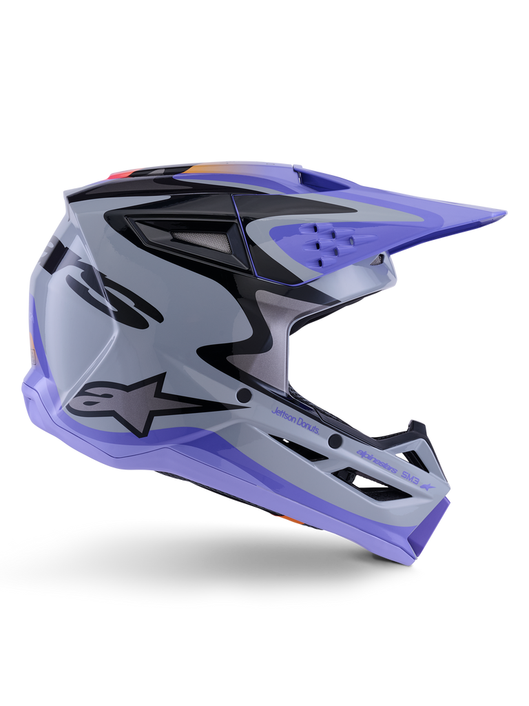 Casco Alpinestars S-M3 Jettson ECE 22.06, casco da motocross, grigio viola e nero lucido, vista di profilo con visiera e mentoniera viola, calotta aerodinamica con grafiche nere, prese d'aria multiple e marchio "Jettson Donuts" sul lato.