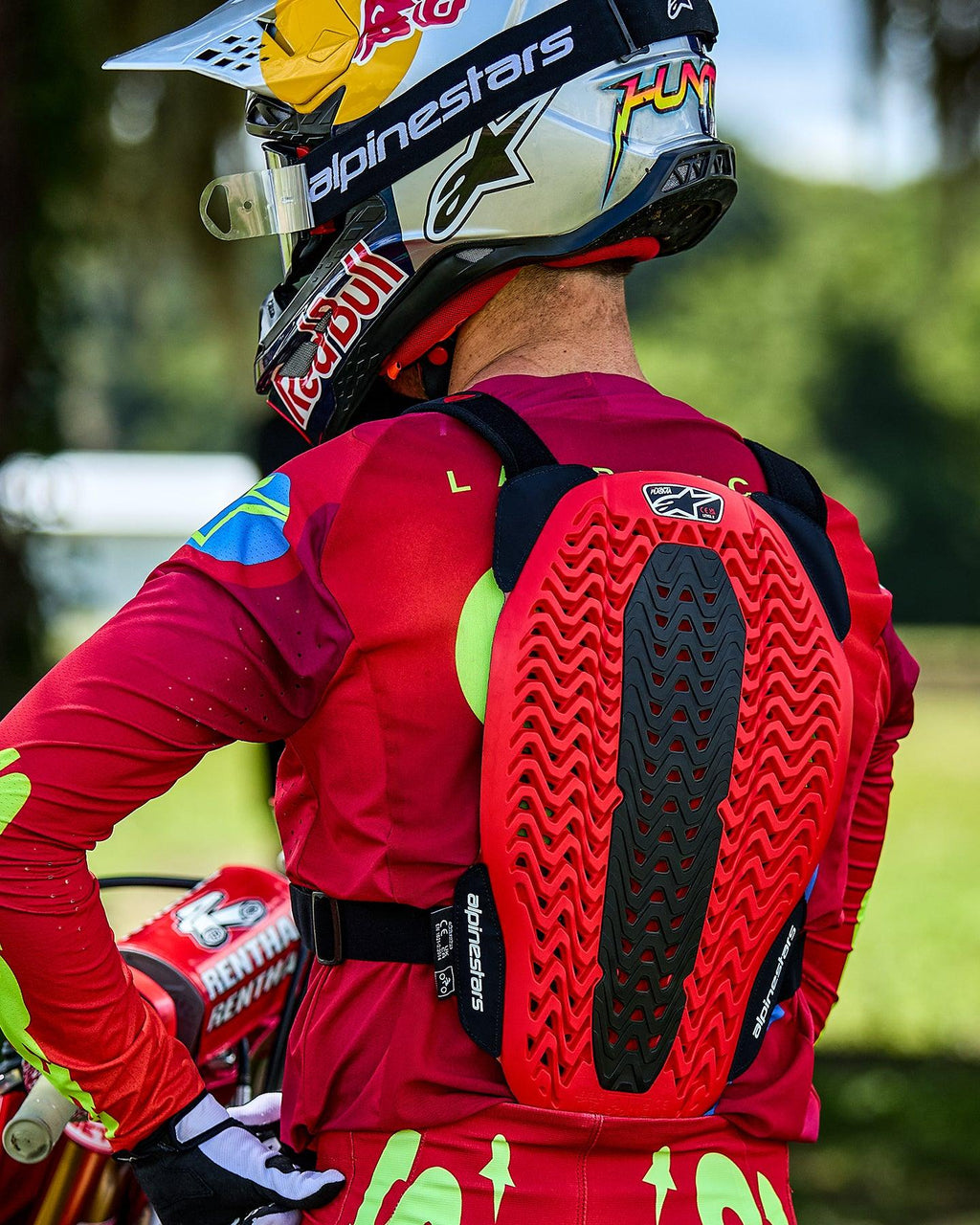 Pilota di motocross visto da dietro che indossa il protettore per torace Alpinestars A-5 Plasma, caratterizzato da un paraschiena rosso e nero con struttura a nido d'ape ventilata, indossato sopra una maglia rossa a maniche lunghe con un casco a marchio Red Bull.