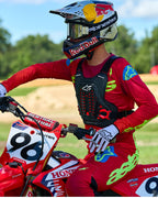 Pilota di motocross con protezione torace Alpinestars A-5 Plasma in nero e rosso, abbinata a maglia e pantaloni da gara rossi e verde lime, seduto su una moto Honda rossa, equipaggiamento protettivo fuoristrada ad alte prestazioni
