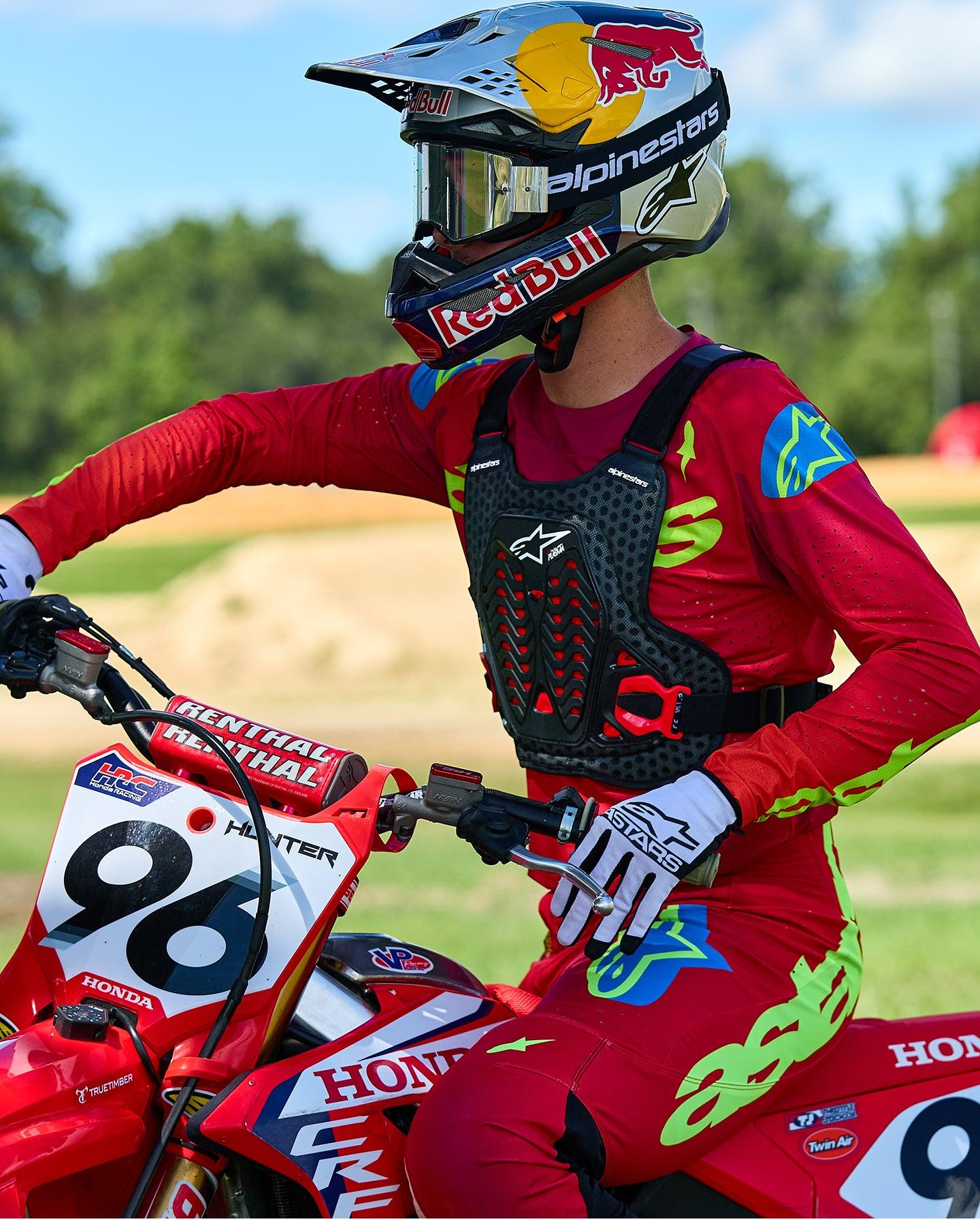 Pilota di motocross con protezione torace Alpinestars A-5 Plasma in nero e rosso, abbinata a maglia e pantaloni da gara rossi e verde lime, seduto su una moto Honda rossa, equipaggiamento protettivo fuoristrada ad alte prestazioni