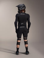 Protezioni ginocchio e tibia Alpinestars A-Impact Plasma Pro, nero, vista posteriore di un rider con attrezzatura protettiva completa da mountain bike, inclusi casco integrale e protezione per il busto, con sistema di chiusura a triplo cinturino e pannelli in rete ventilata per una vestibilità sicura e circolazione dell'aria