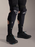 Ginocchiere Alpinestars A-Impact Plasma Pro, nero e bianco, con logo della tecnologia Nucleon PLASMA, indossate con calze nere e scarpe da mountain bike nere, chiusure a strappo sicure, equipaggiamento protettivo ergonomico per ciclismo fuoristrada