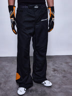Alpinestars RSRV Arena Suit Pants, pantaloni da corsa neri con loghi McLaren e Alpinestars, dettagli arancioni, indossati con guanti racing neri e arancioni e scarpe bianche con accenti neri
