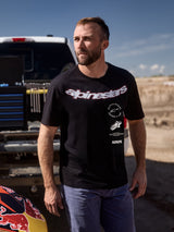 T-shirt Alpinestars Abus CSF, maglietta a maniche corte, nero, con grande marchio Alpinestars curvo e loghi sovrapposti, indossata da un uomo in un paddock, stile casual streetwear