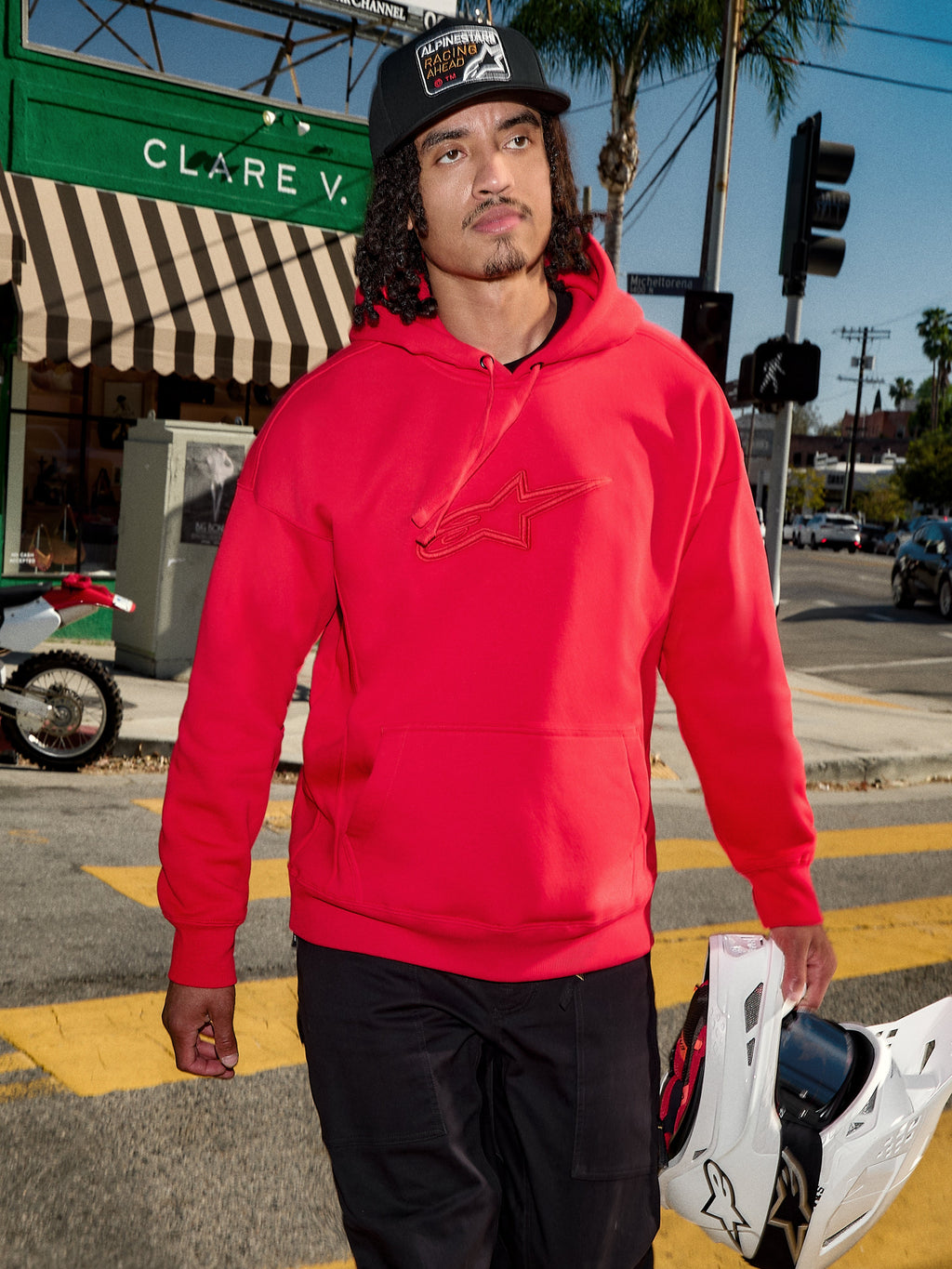 Alpinestars Emergent Oversized Hoodie, rosso, logo Astars ricamato in 3D sul petto, indossata con pantaloni neri e un cappellino da baseball mentre porta un casco da motocross bianco, stile casual urban streetwear