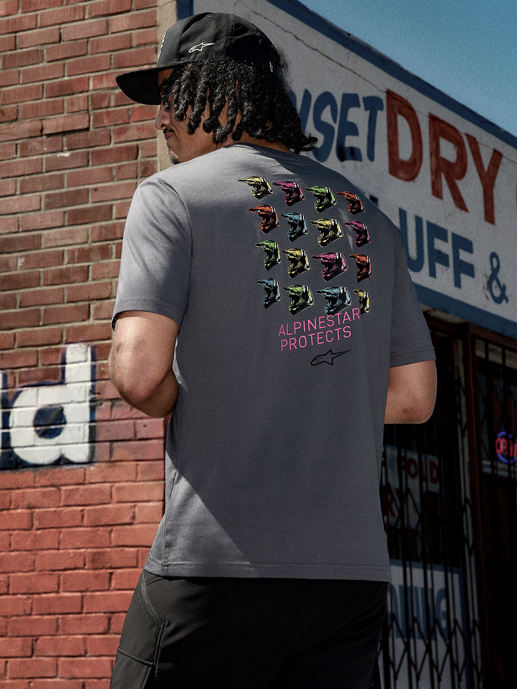 Alpinestars Pop Helmet CSF Tee, maglietta a maniche corte, grigio antracite, grafica sul retro con caschi M10 colorati e scritta rosa "ALPINESTAR PROTECTS", streetwear casual ispirato al motorsport