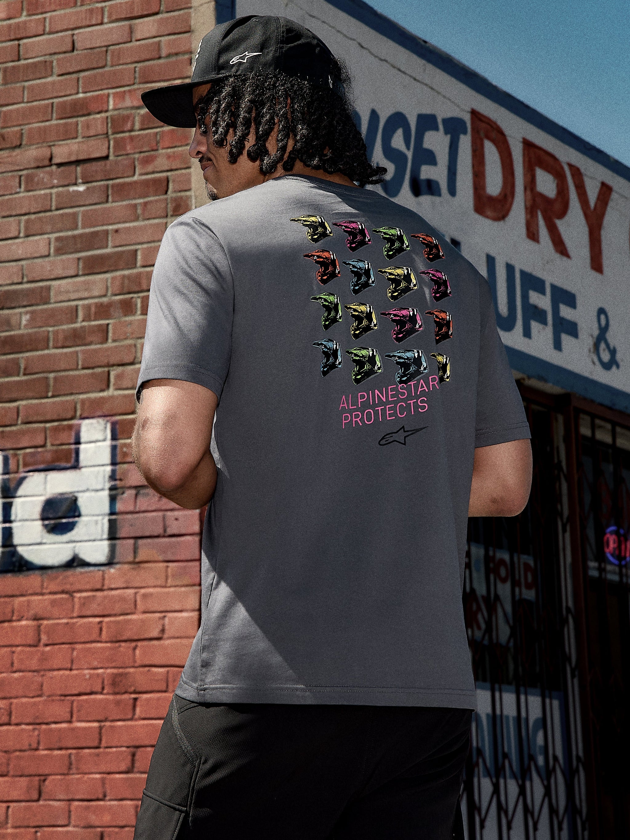 Alpinestars Pop Helmet CSF Tee, maglietta a maniche corte, grigio antracite, grafica sul retro con caschi M10 colorati e scritta rosa "ALPINESTAR PROTECTS", streetwear casual ispirato al motorsport