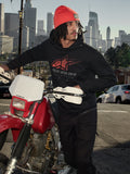 Alpinestars Pulse Hoodie, felpa con cappuccio, nera con logo Astars Combo rosso e grigio, indossata da un uomo con berretto arancione accanto a una motocicletta Honda rossa in un contesto urbano, streetwear casual motorsport