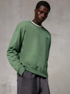 Alpinestars Essentials Ageless Crew, felpa girocollo, verde cactus, con un piccolo logo Alpinestars nero sul petto, indossata da un modello con pantaloni grigi, stile casual lifestyle streetwear