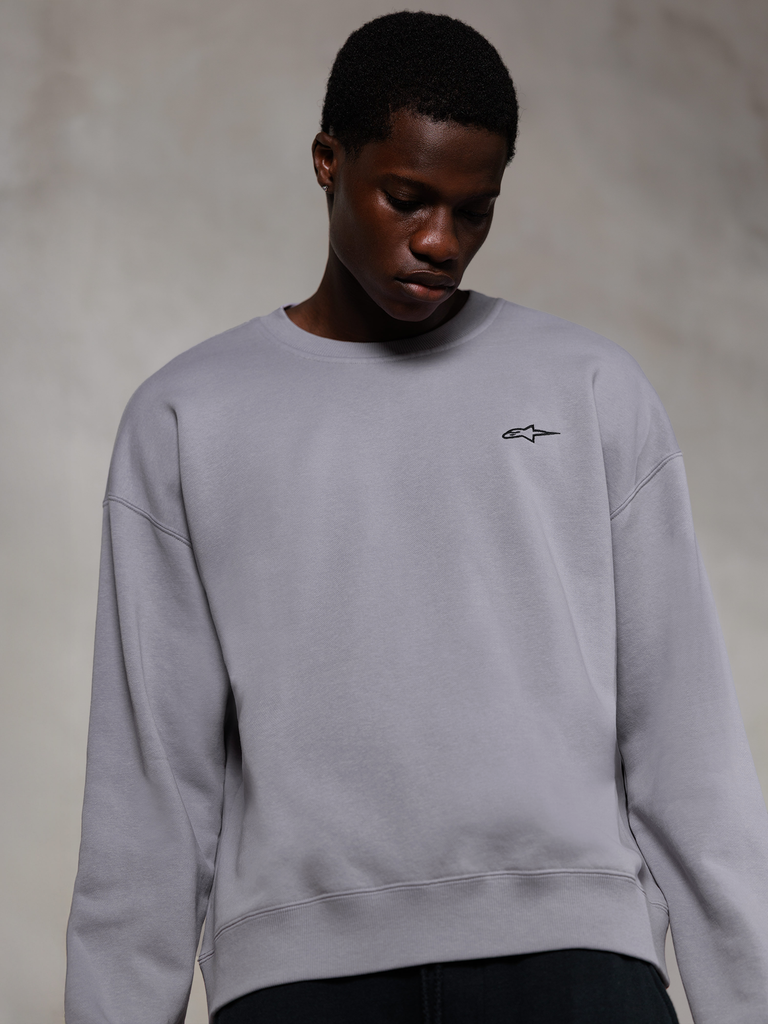 Alpinestars Essentials Ageless Crew, felpa girocollo premium color argento, con un piccolo logo Alpinestars nero sul petto, indossata da un modello, stile streetwear casual con consistenza in morbido pile.