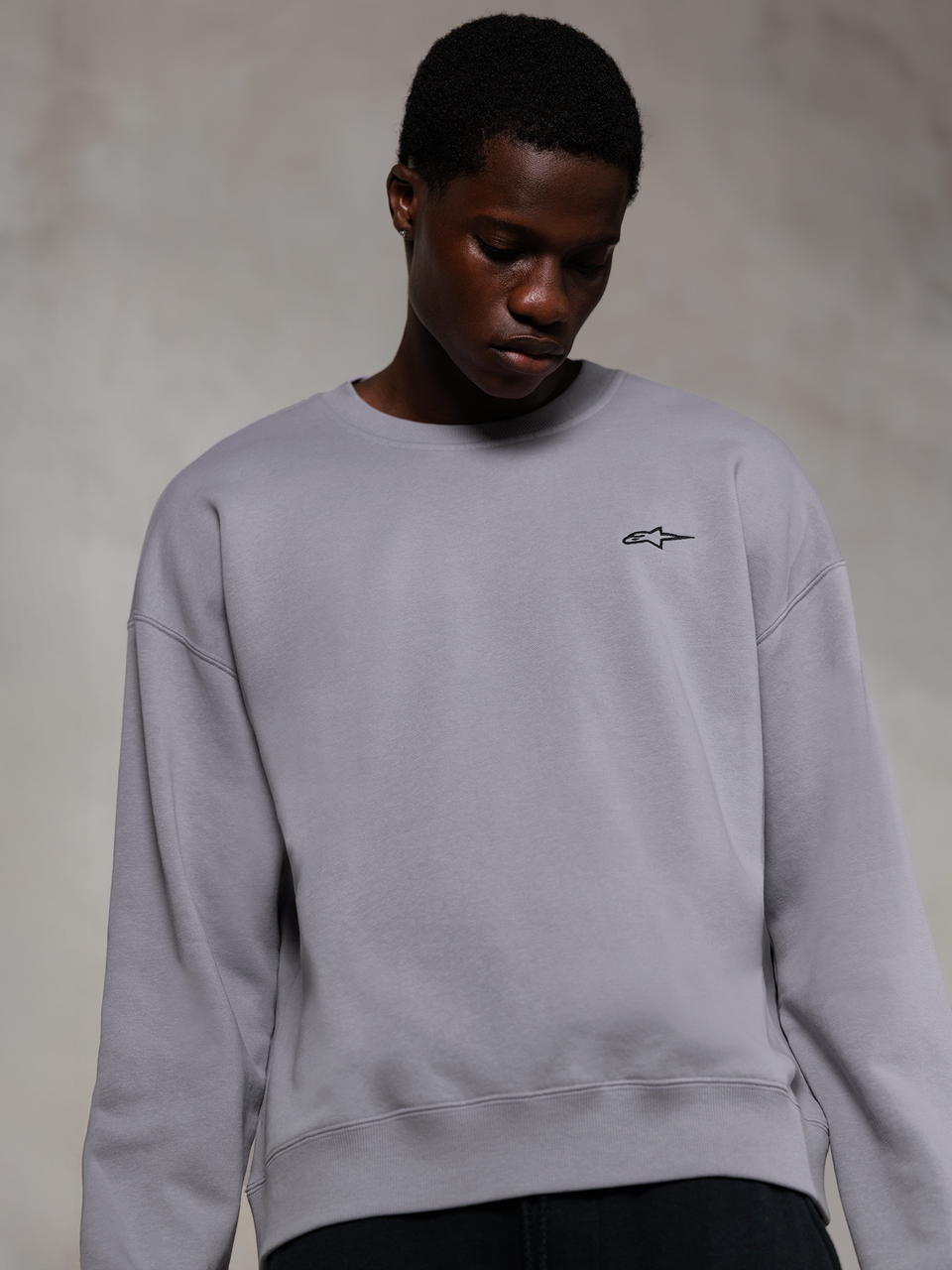 Alpinestars Essentials Ageless Crew, felpa girocollo premium color argento, con un piccolo logo Alpinestars nero sul petto, indossata da un modello, stile streetwear casual con consistenza in morbido pile.