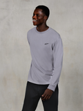 Alpinestars Essentials Ageless LS Tee, maglietta a maniche lunghe, Silver, piccolo logo nero sul petto, indossata da un modello sorridente con pantaloni scuri, vestibilità rilassata contemporanea, abbigliamento casual motorsport lifestyle