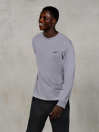 Alpinestars Essentials Ageless LS Tee, maglietta a maniche lunghe, Silver, piccolo logo nero sul petto, indossata da un modello sorridente con pantaloni scuri, vestibilità rilassata contemporanea, abbigliamento casual motorsport lifestyle