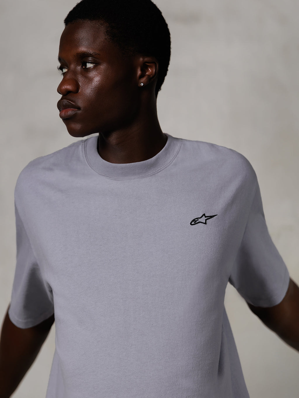 Modello che indossa Alpinestars Essentials Ageless SS Tee, maglietta a maniche corte, Silver, con un piccolo logo nero sul petto, vestibilità rilassata, design streetwear pulito e minimale