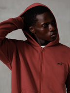 Alpinestars Essentials Ageless Zip Hoodie, rosso mattone, lifestyle streetwear casual, cappuccio alzato con mano dietro la testa, piccolo logo Astars nero sul petto, felpa in pile dalla vestibilità rilassata