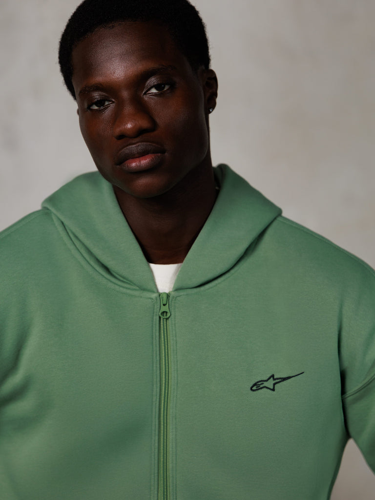 Alpinestars Essentials Ageless Zip Hoodie, ritratto lifestyle, verde cactus con piccolo logo nero, apertura frontale con zip, consistenza in morbido pile, streetwear casual d'ispirazione motorsport