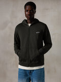 Alpinestars Essentials Ageless Zip Hoodie, Off Black, felpa con cappuccio e zip con un piccolo logo Alpinestars bianco sul petto, vestibilità rilassata, indossata da un modello con jeans blu e una t-shirt bianca, streetwear casual ispirato al motorsport