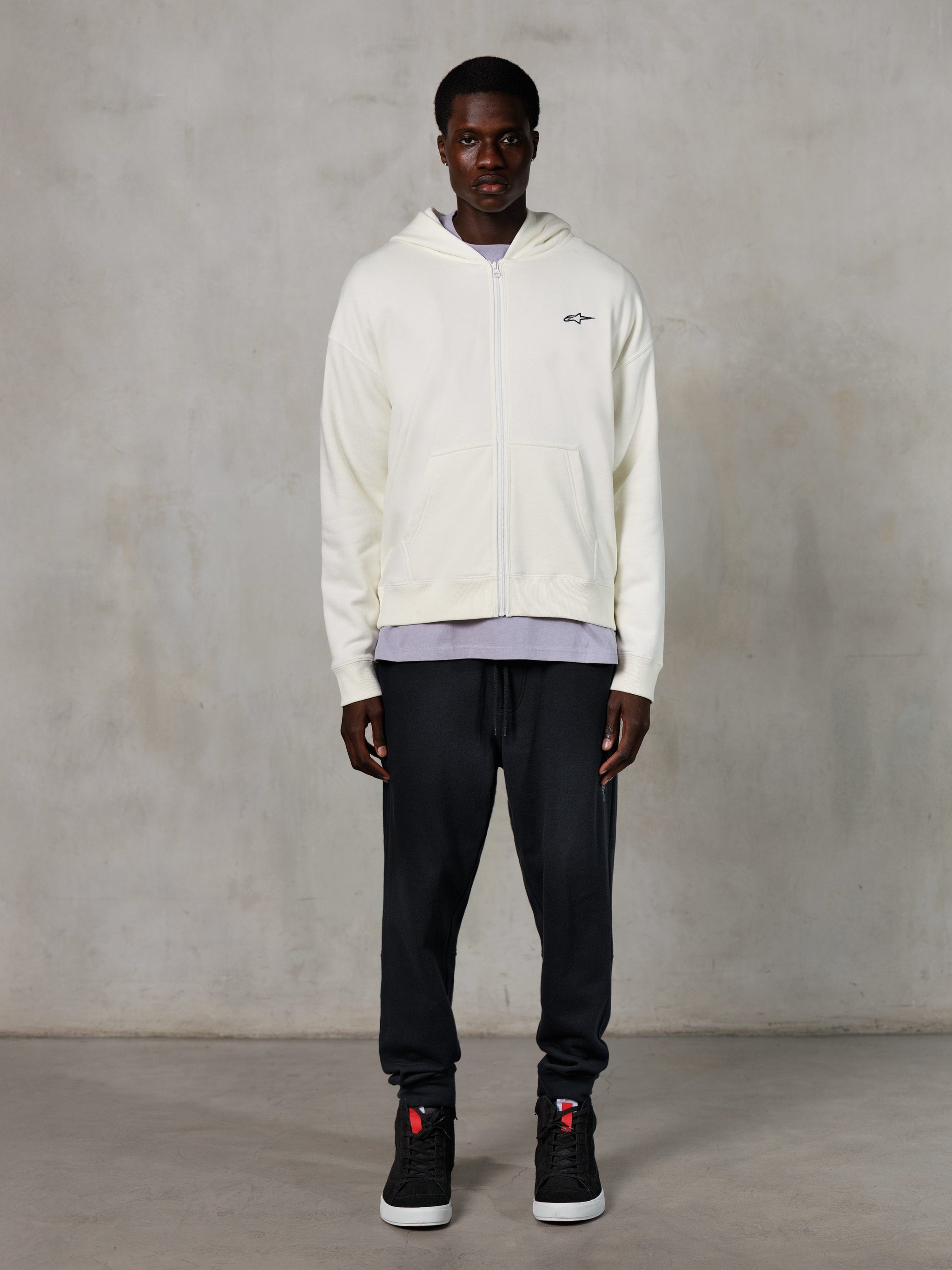 Felpa con cappuccio e zip Alpinestars Essentials Ageless, streetwear casual, bianco sporco con discreto logo nero sul petto, chiusura frontale con zip, design con cappuccio, vestibilità rilassata, abbinata a pantaloni sportivi neri e sneakers