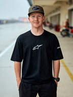 Uomo con t-shirt Alpinestars Frontal CSF, maglietta a maniche corte nera, logo Astars centrale bianco, cappellino Alpinestars verde oliva, streetwear casual ispirato al motorsport