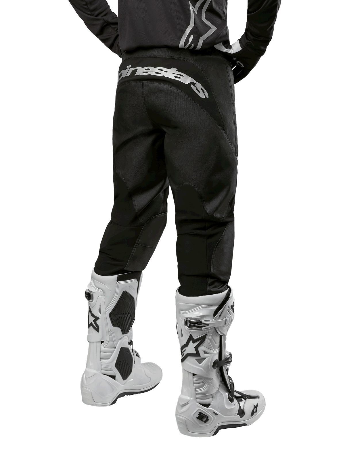 Alpinestars Pantaloni Fluid Graphite 2024, pantaloni da motocross, nero e argento, vista posteriore con logo Alpinestars argento sul carré, indossati con stivali da motocross bianchi e neri, design in tessuto resistente per la guida fuoristrada