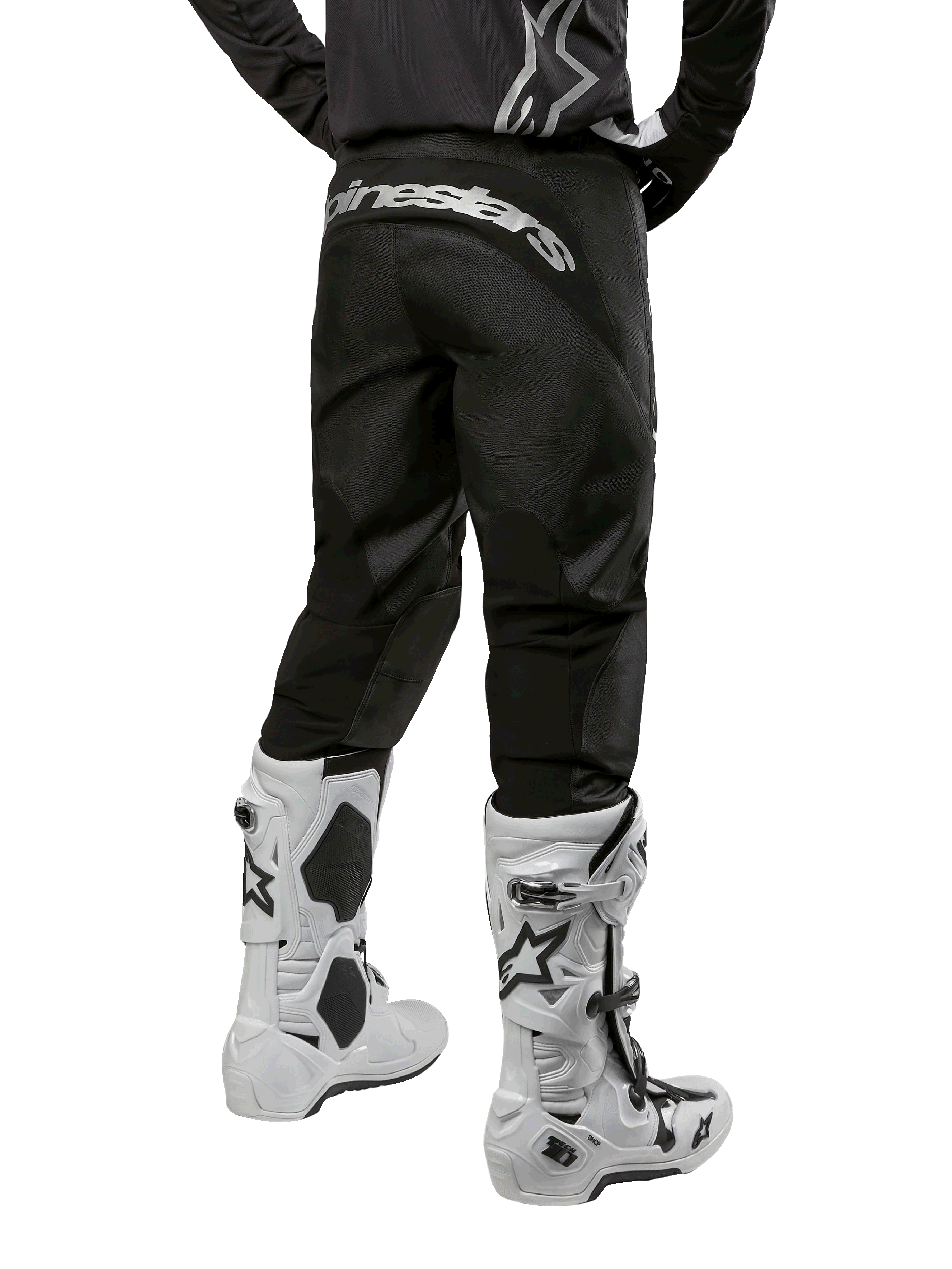 Alpinestars Pantaloni Fluid Graphite 2024, pantaloni da motocross, nero e argento, vista posteriore con logo Alpinestars argento sul carré, indossati con stivali da motocross bianchi e neri, design in tessuto resistente per la guida fuoristrada