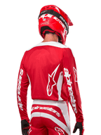 Pilota di motocross con maglia Alpinestars Fluid Lurv 2024, rosso Marte e bianco, vista posteriore con logo Alpinestars bianco sulla schiena e marchio sulle maniche, abbinata a casco rosso e guanti neri, abbigliamento professionale da corsa off-road