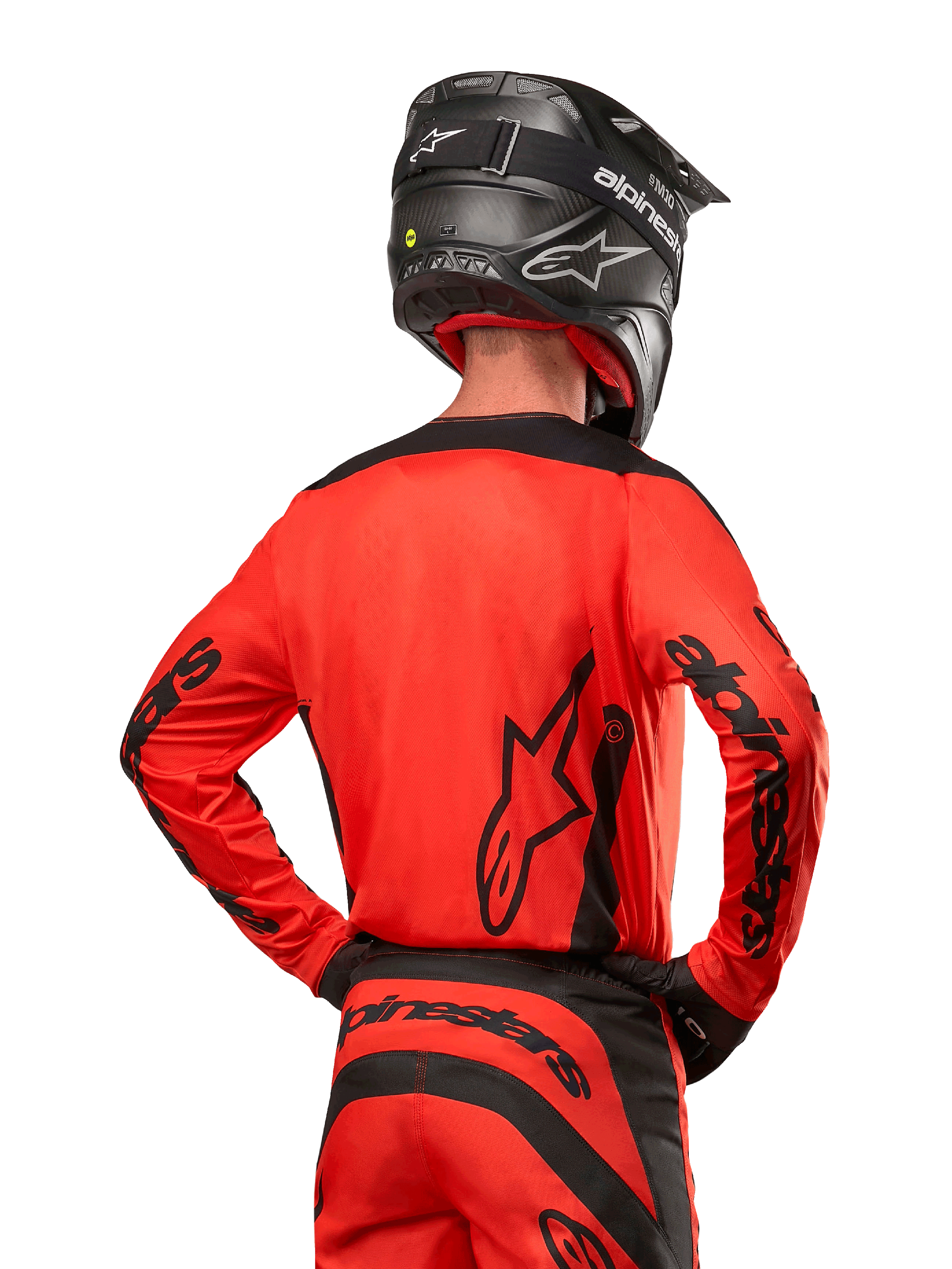 Pilota di motocross visto da dietro con maglia Alpinestars Fluid Lurv 2024 in Hot Orange e nero, loghi Alpinestars su schiena e maniche, abbinata a pantaloni da motocross coordinati e casco nero, progettata per prestazioni off-road.