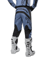 Alpinestars 2024 Fluid Lurv Pants, pantaloni da motocross, azzurro e nero, vista posteriore che mostra pannelli rinforzati neri e un grande logo del marchio, abbinati a stivali da motocross bianchi e neri, equipaggiamento professionale per fuoristrada