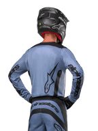 Alpinestars 2024 Fluid Lurv Jersey, maglia da motocross, azzurro e nero, vista posteriore del pilota che mostra il grande logo a stella e il branding sulle maniche, indossata con casco nero e pantaloni da fuoristrada coordinati, abbigliamento racing professionale