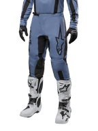 Pantaloni Alpinestars Fluid Lurv 2024, pantaloni da motocross blu chiaro e nero, indossati con maglia a maniche lunghe coordinata e stivali da motocross bianchi, caratterizzati da un evidente logo a stella nero sulla coscia e pannelli interni rinforzati sulle ginocchia, vista frontale su sfondo bianco.