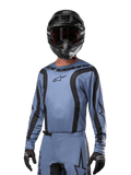 Pilota di motocross con maglia Alpinestars 2024 Fluid Lurv, azzurro e nero, abbinata a casco e occhiali neri, con grafiche nere e logo a stella Alpinestars, abbigliamento tecnico per gare fuoristrada