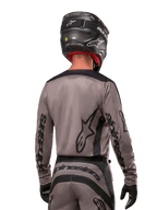 Pilota di motocross visto di spalle che indossa la maglia Alpinestars Fluid Lurv 2024 in Mud Black, con branding Alpinestars nero su maniche e schiena, abbinata a casco nero e attrezzatura per corse fuoristrada
